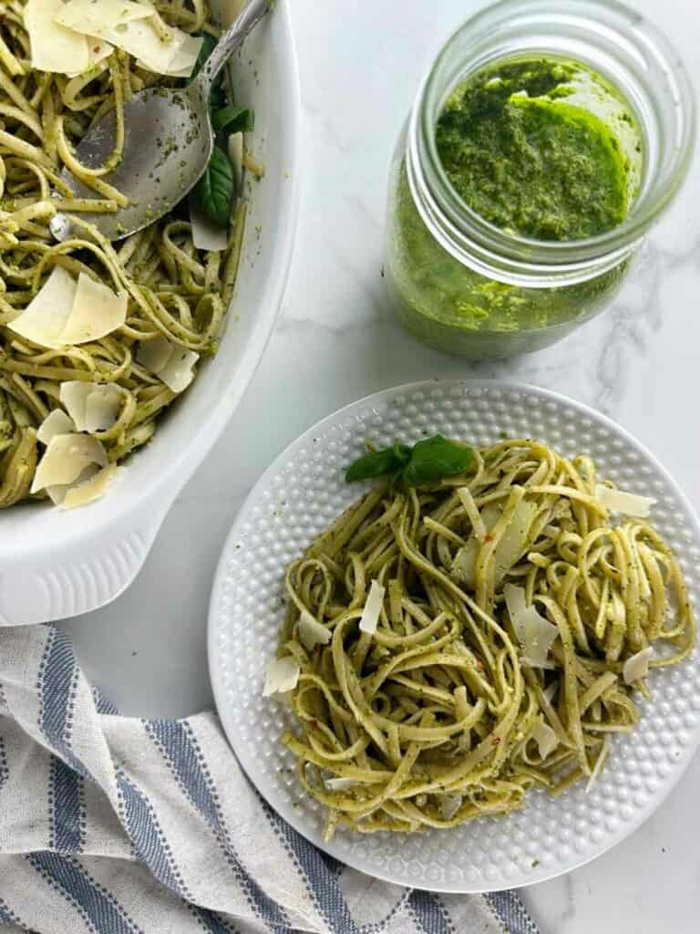 A plate of pasta al pesto near a serving dish of pesto pasta