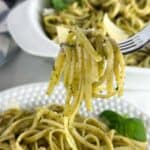 Fork full of pasta al pesto with bowls of the pasta in the background.