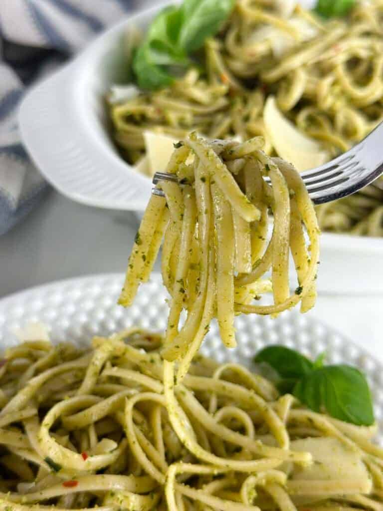 Fork full of pasta al pesto with bowls of the pasta in the background.