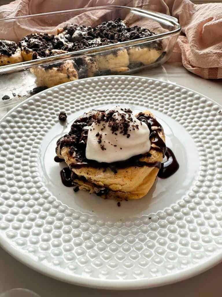 Single Oreo cinnamon bun on a serving plate with chocolate syrup and whipped cream topping.