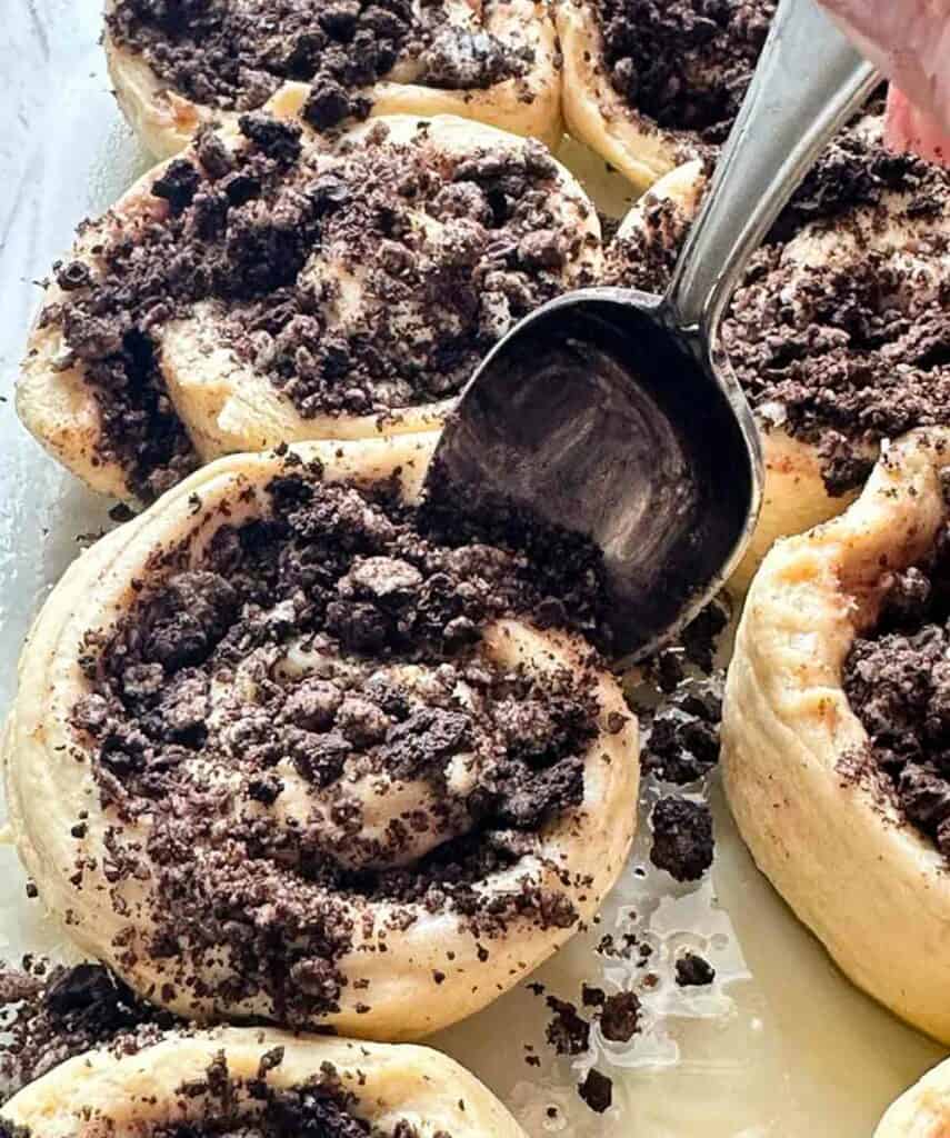 Stuffing Oreo cookies into cinnamon buns with a spoon.