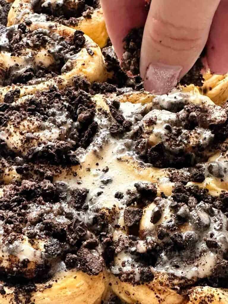 Topping iced Oreo cinnamon buns with some additional cookie crumbles.