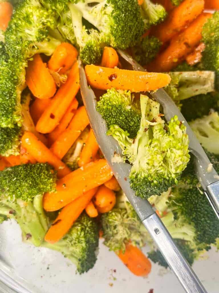 Tossing broccoli and carrots with tongs to get them ready to roast.