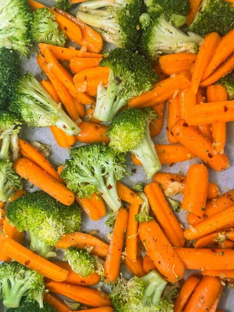 Tossed broccoli and carrots spread on a parchment paper lined baking sheet.