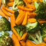 Fully roasted broccoli and carrots still on a parchment lined baking sheet.