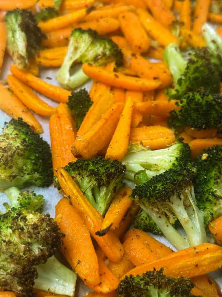 Fully roasted broccoli and carrots still on a parchment lined baking sheet.