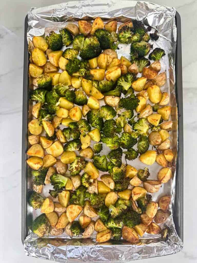 Roasted potatoes with broccoli on an aluminum foil lined baking sheet.