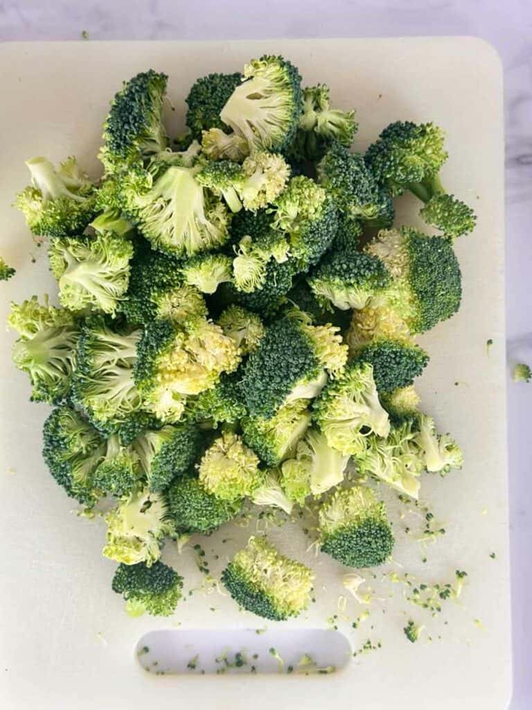 Broccoli crowns on a white cutting board.