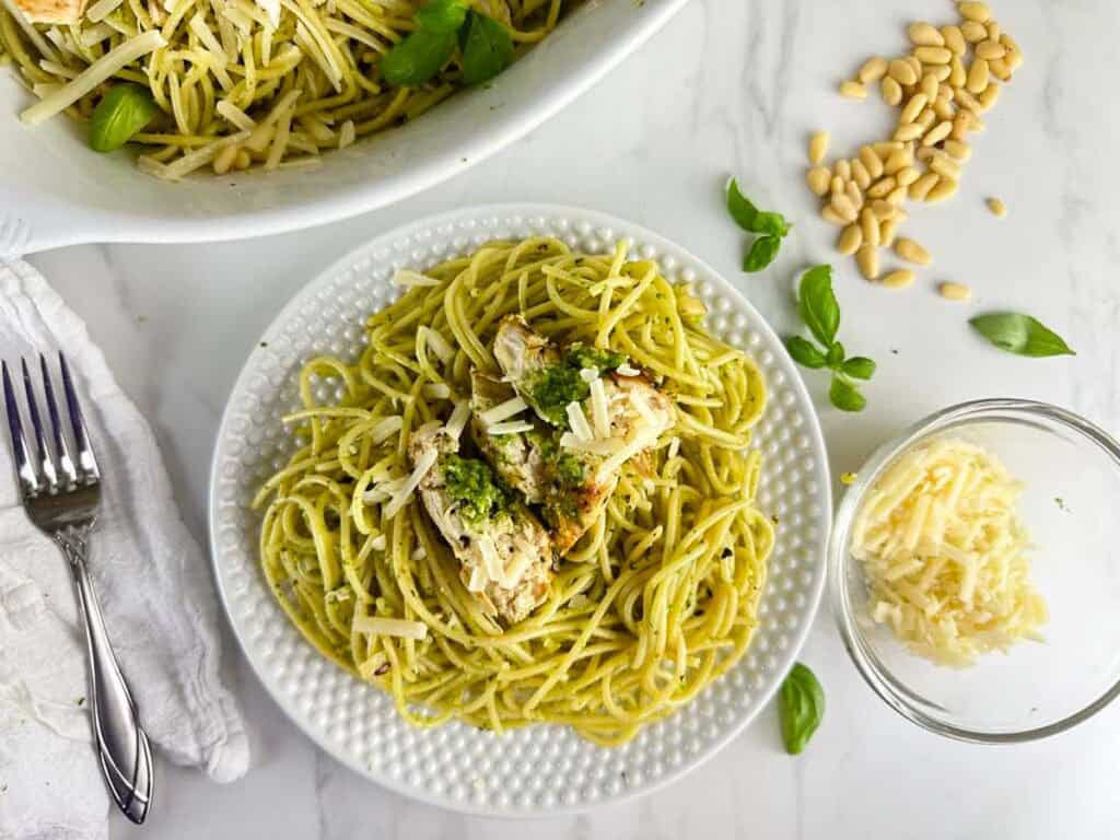 Chicken Spaghetti Pesto on a plate next to a serving platter full of chicken pesto pasta