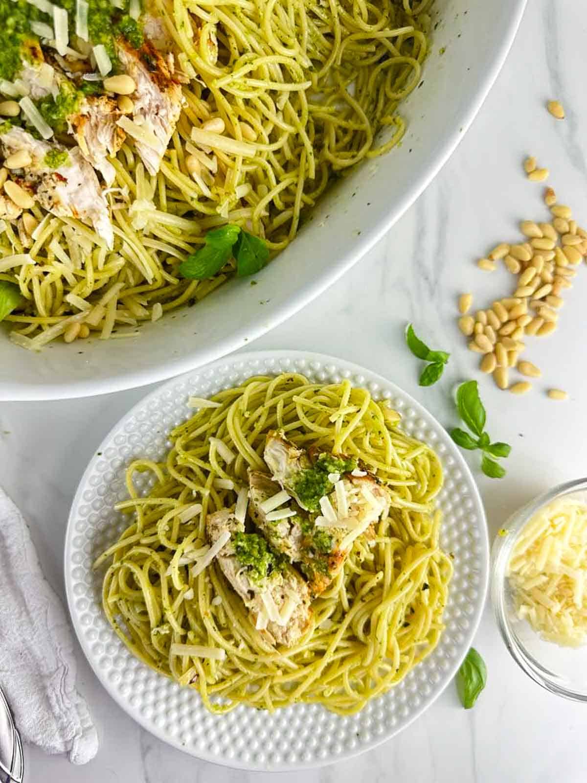 Chicken Spaghetti Pesto on a plate next to a serving platter full of chicken pesto pasta