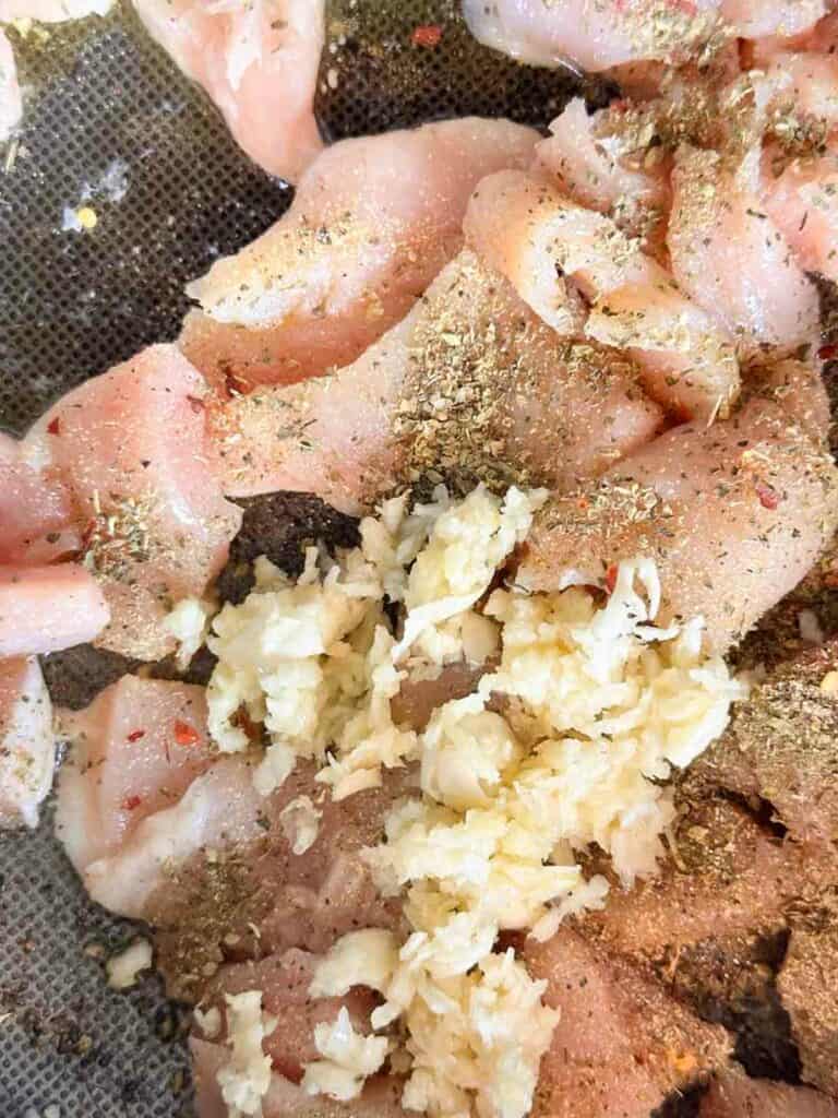 Seasoned chicken pieces in a saute pan with crushed garlic