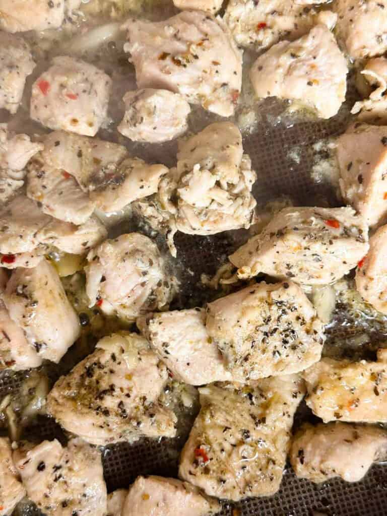 Seasoned chicken pieces in a saute pan with crushed garlic