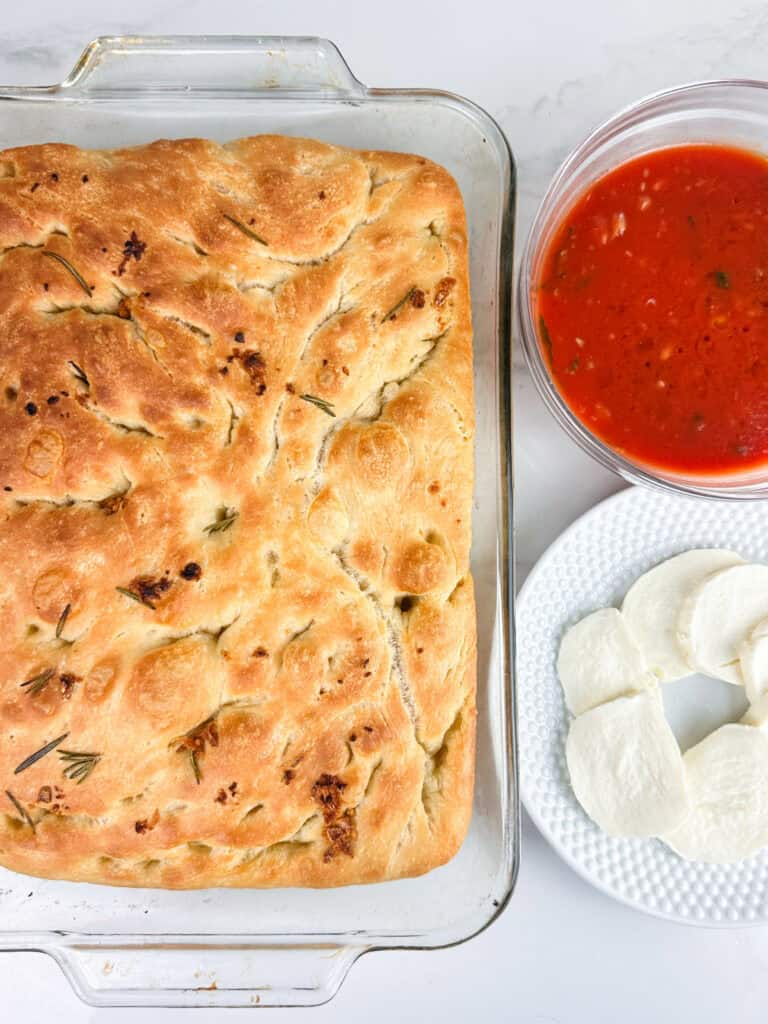 Focaccia bread, tomato sauce, and fresh mozzarella on a neutral background.