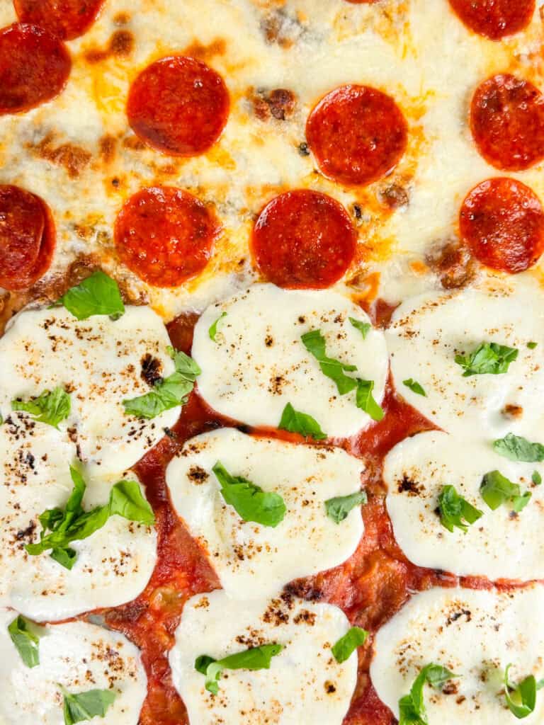 Baked focaccia bread pizza with pepperoni and fresh basil added on top.