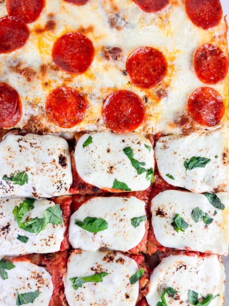 Baked focaccia bread pizza with pepperoni and fresh basil added on top.