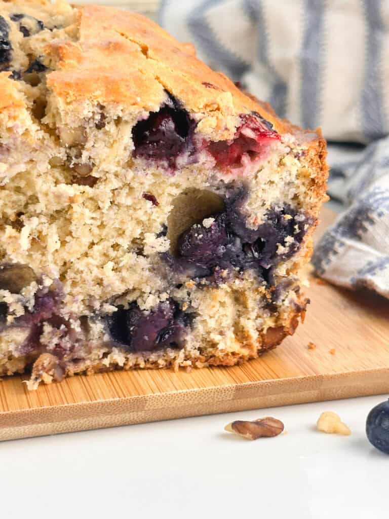 A loaf of blueberry banana nut quick bread with the end cut off to show the moist crumb and how loaded with berries it is