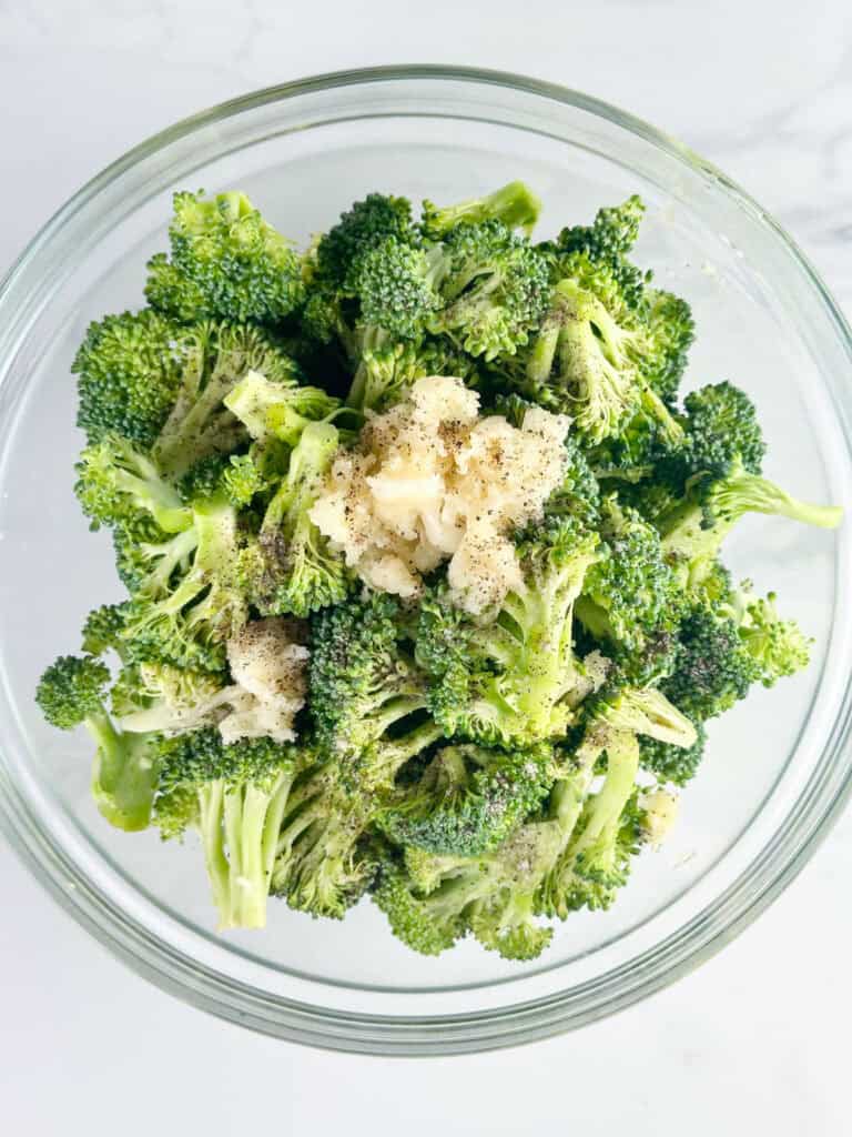 Broccoli aand garlic in a clear bowl on a white background.