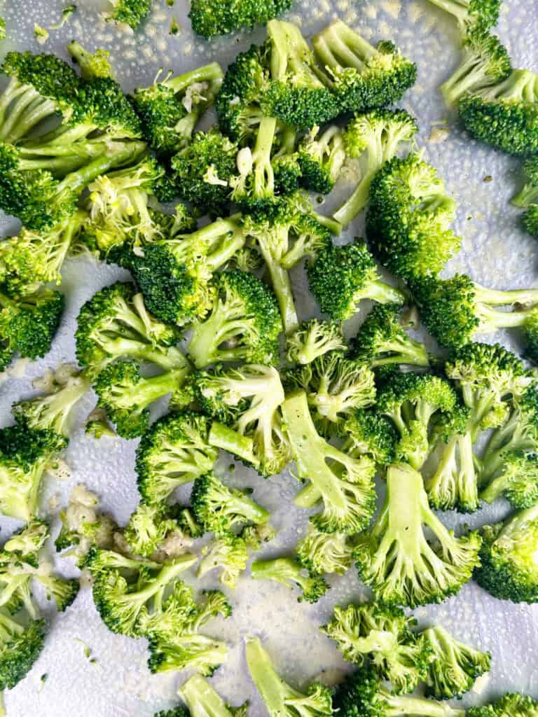 Broccoli spread out on a aluminum lined baking sheet.