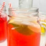 Text reads raspberry lemonade cocktail over an image of a mason jar containing a red and white straw and the cocktail.