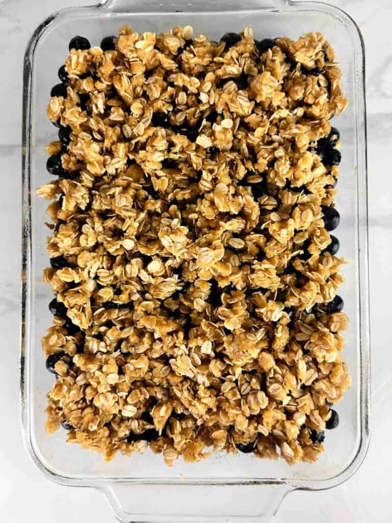 Oat and brown sugar topping on blueberries in a clear baking dish.