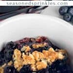 Blueberry crumble serving in a white bowl. Text reads: blueberry crumble seasonedsprinkles.com