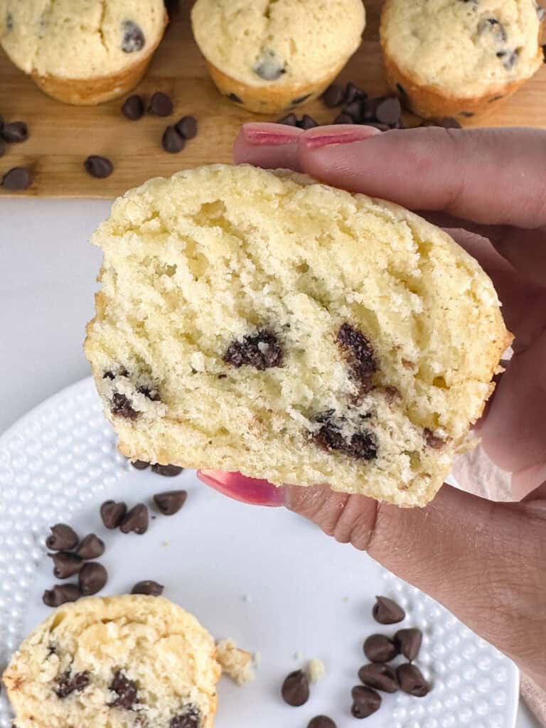 Ready to eat chocolate chip muffin with buttermilk held in hand over other muffins.