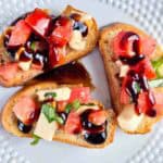 Caprese bruschetta with a balsamic drizzle on a white plate.