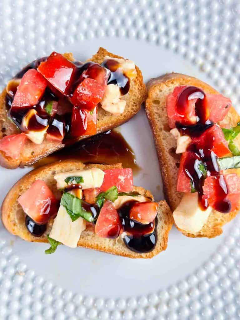 Caprese bruschetta with a balsamic drizzle on a white plate.