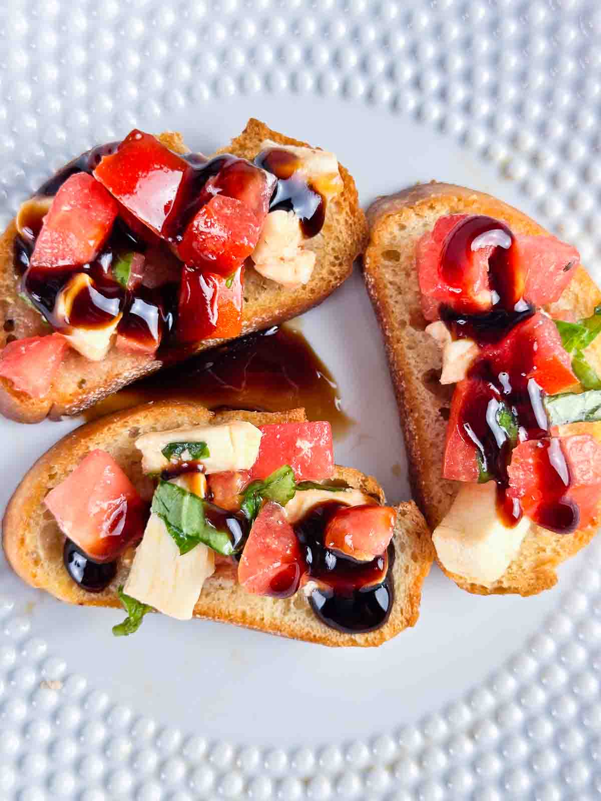 Caprese bruschetta with a balsamic drizzle on a white plate.