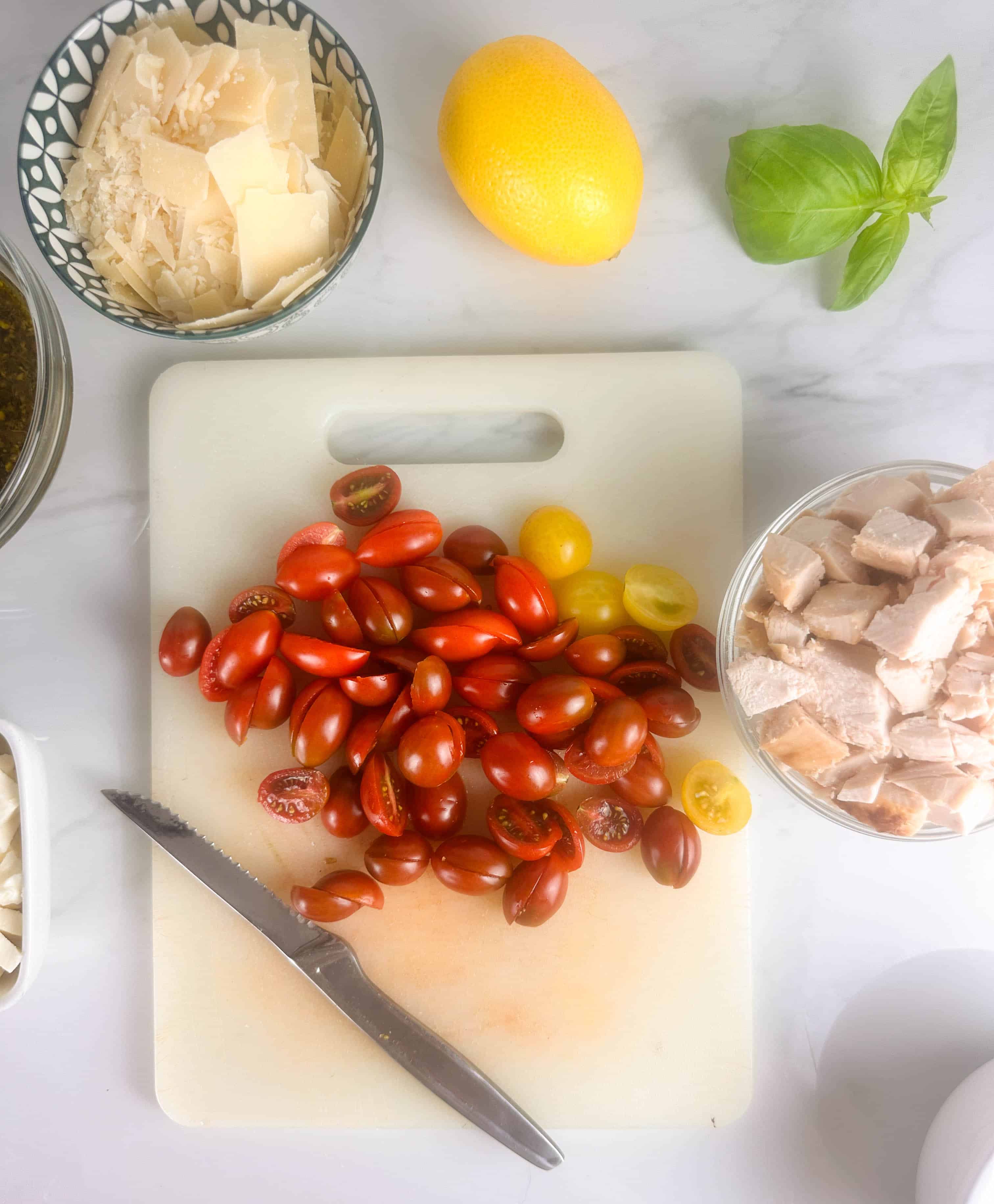 Chopping cherry tomatoes in half on a white cutting board with other ingredients around it.