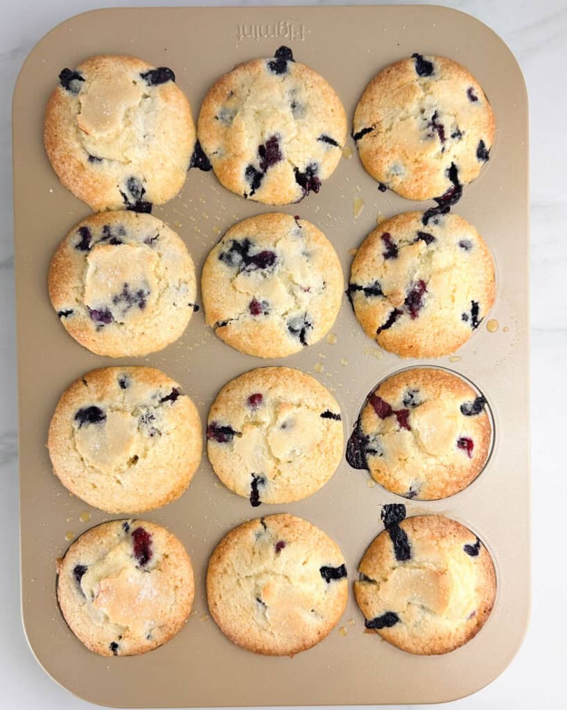 Fully baked buttermilk blueberry muffins in a gold colored muffin tin.