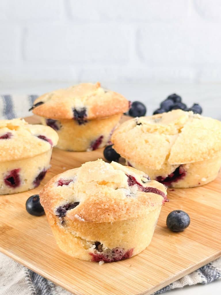 Fully baked buttermilk blueberry muffins on a wood cutting board.