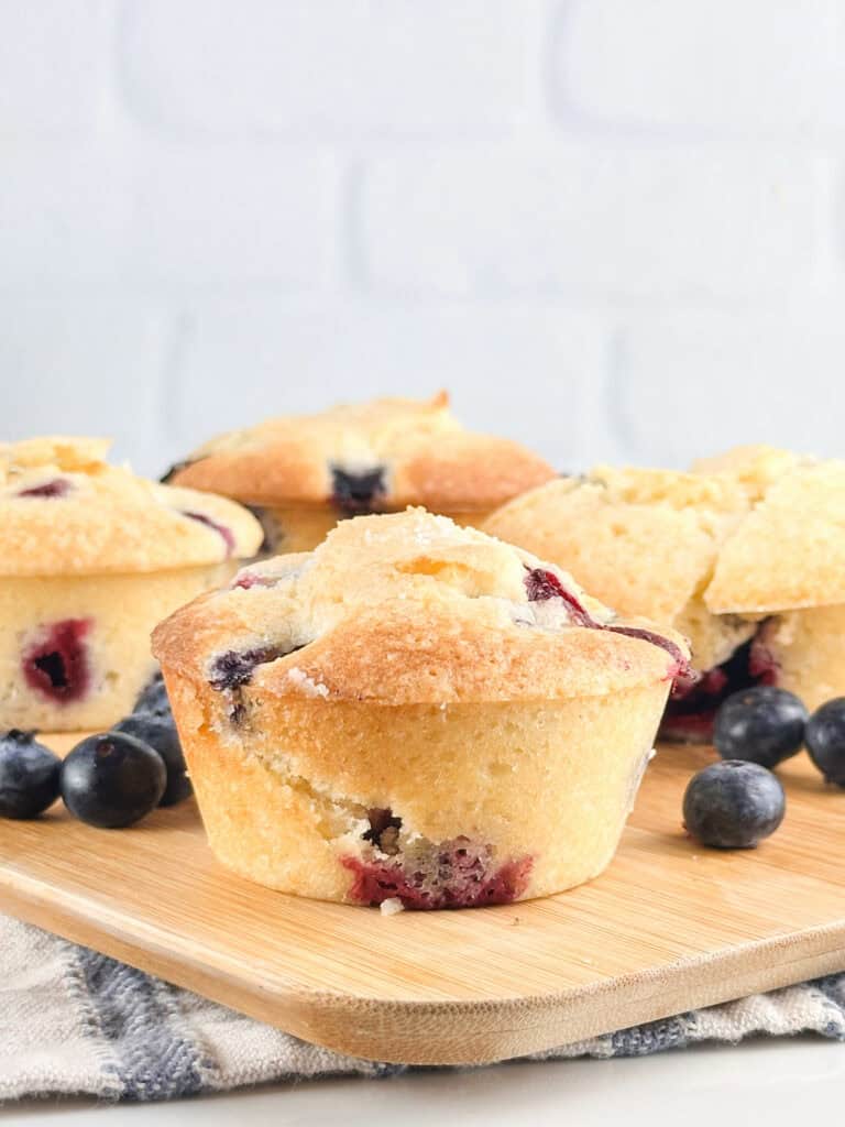 Fully baked buttermilk blueberry muffins on a wood cutting board.