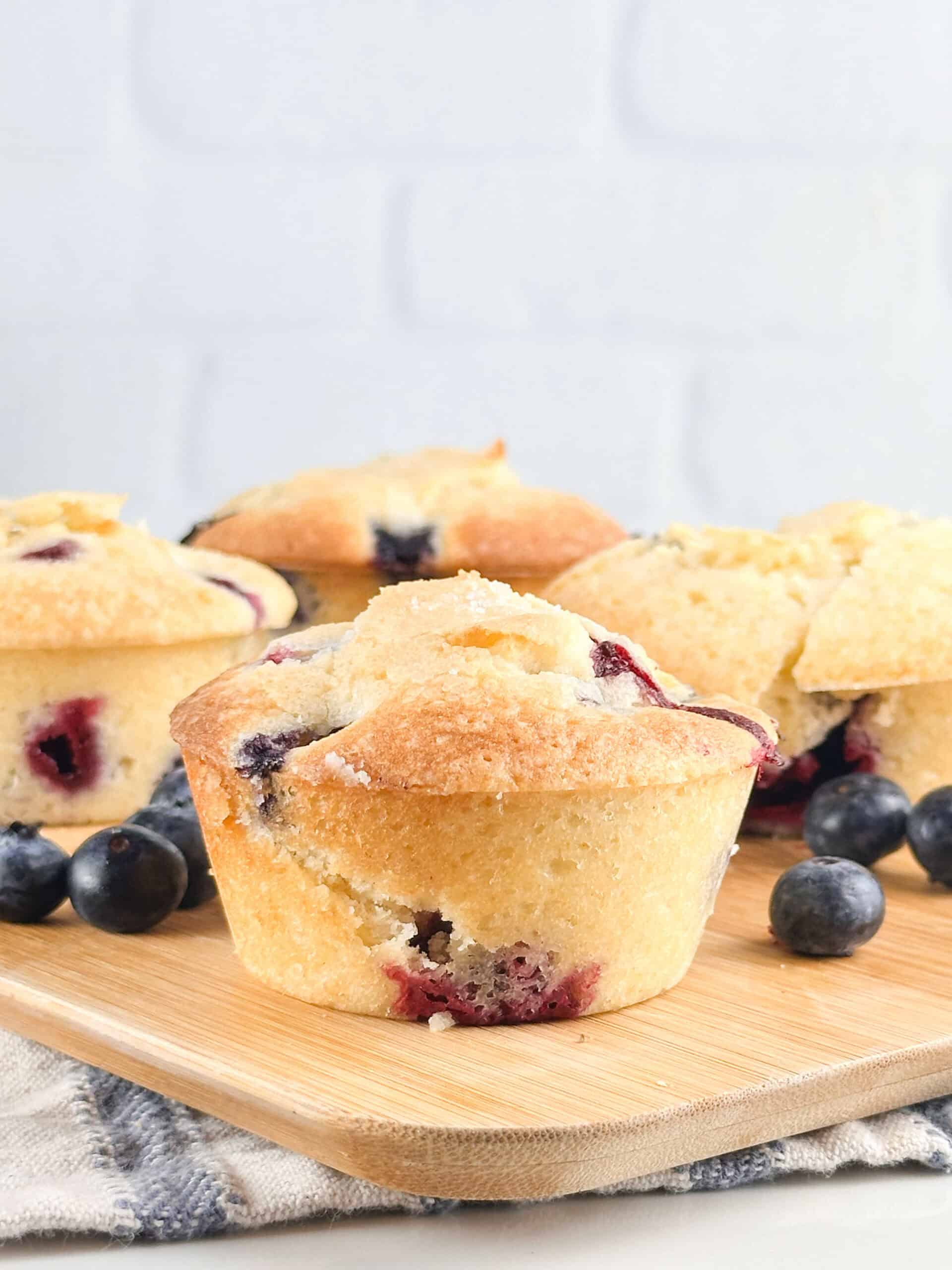 Fully baked buttermilk blueberry muffins on a wood cutting board.