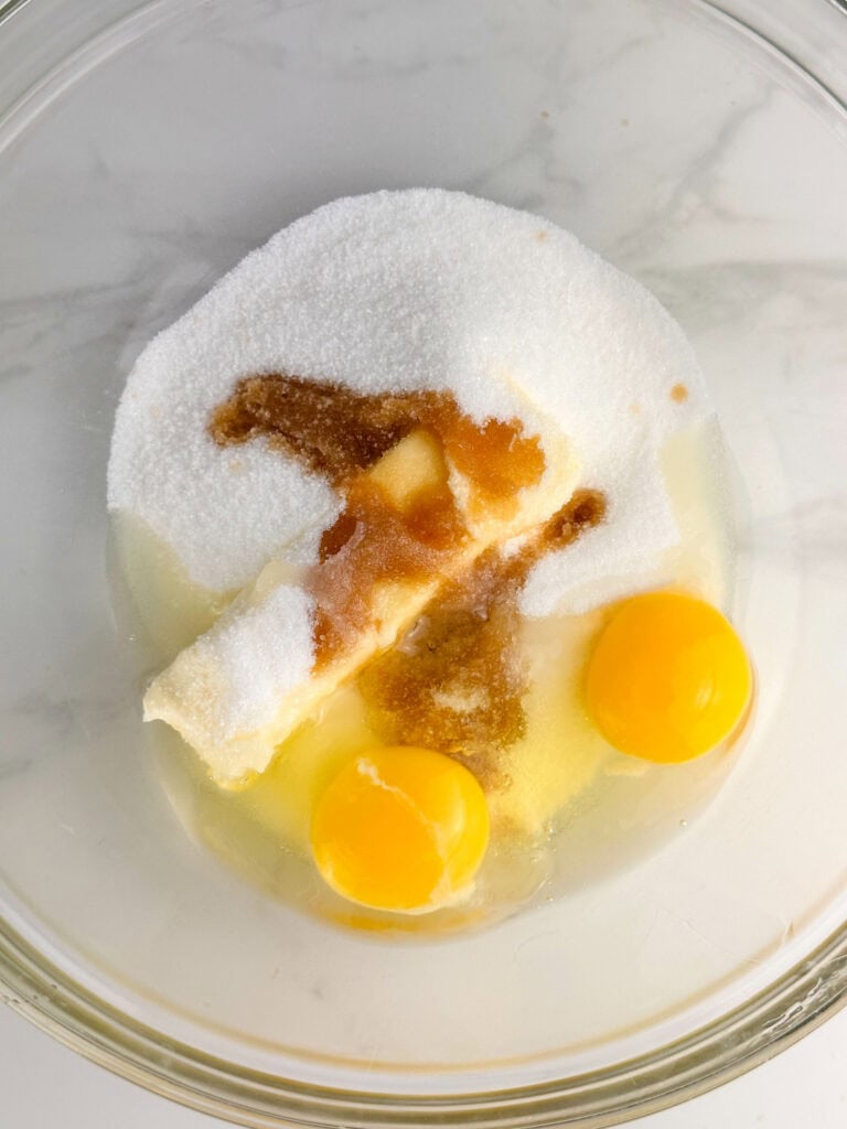 Eggs, butter, vanilla extract, and sugar in a clear mixing bowl.