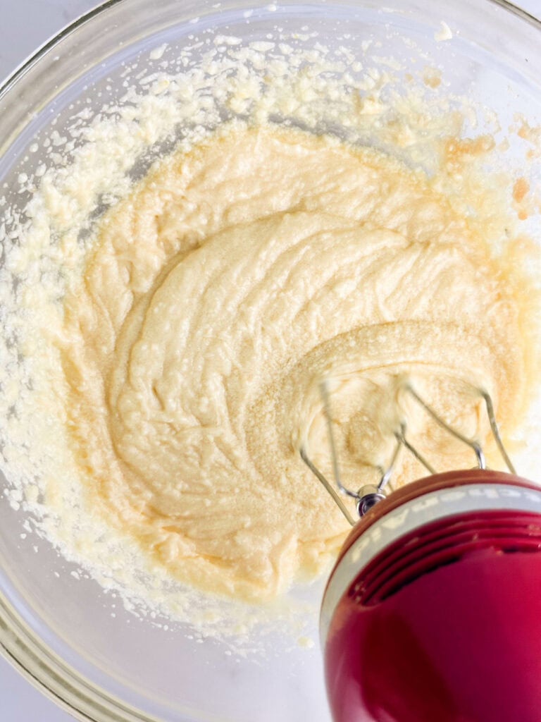 Creaming butter and sugar in a clear mixing bowl with a red hand mixer.