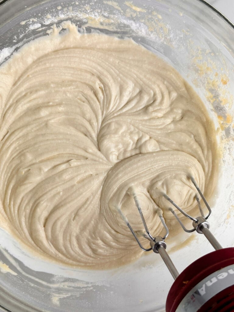 Mixed buttermilk blueberry muffin batter in a clear bowl using a red hand mixer.