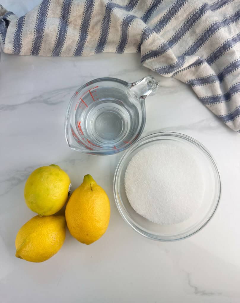 Ingredients for homemade lemonade recipe: lemons, sugar, and water set on a white background.