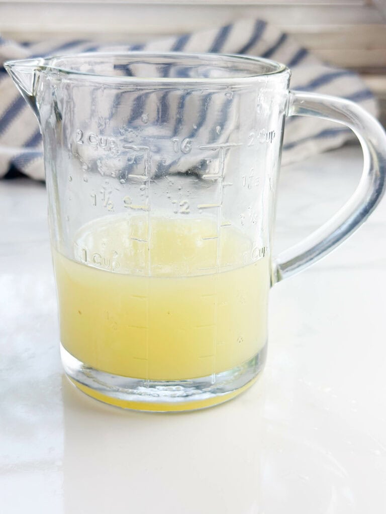 A clear measuring cup with about 1 cup of lemon juice.