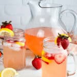 Two glasses and a pitcher of strawberry lemonade on a neutral background.