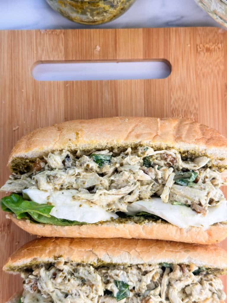 Two rolls of pesto chicken salad with mozzarella cheese on a wood cutting board.