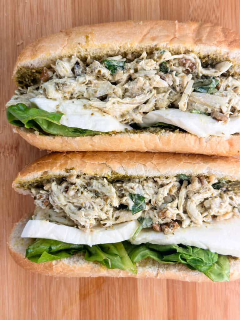 Two rolls of pesto chicken salad with mozzarella cheese on a wood cutting board.