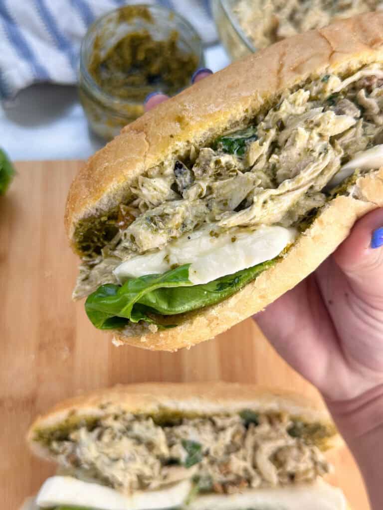 Hand holding pesto chicken salad sandwich over a cutting board with another sandwich on it.