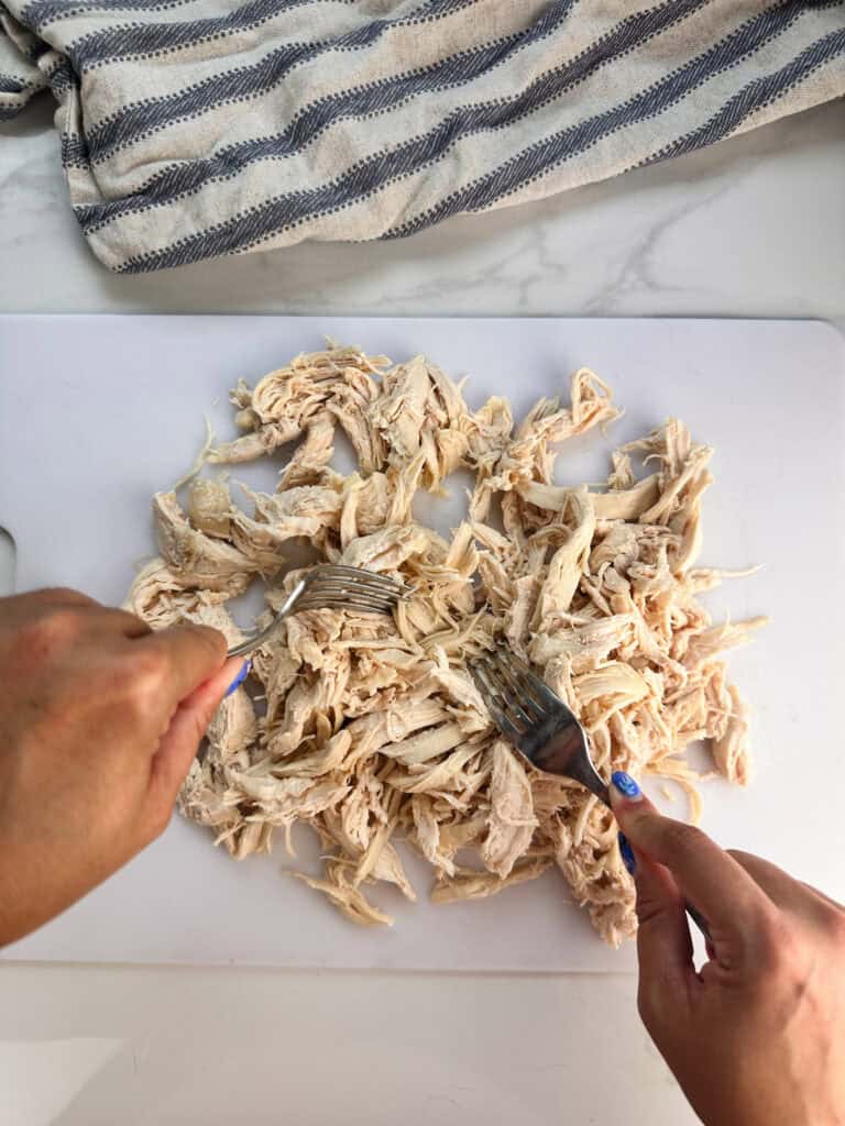 Shredding chicken on a white cutting board using two forks.