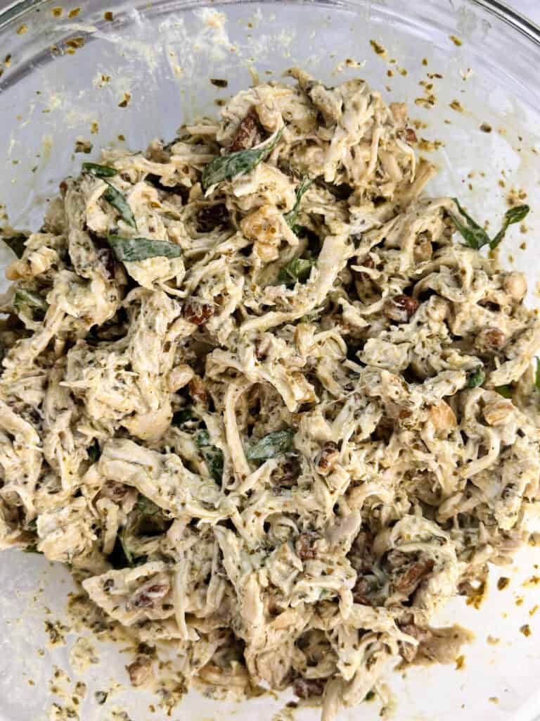 Fully mixed pesto chicken salad ready to serve or store in a clear bowl.