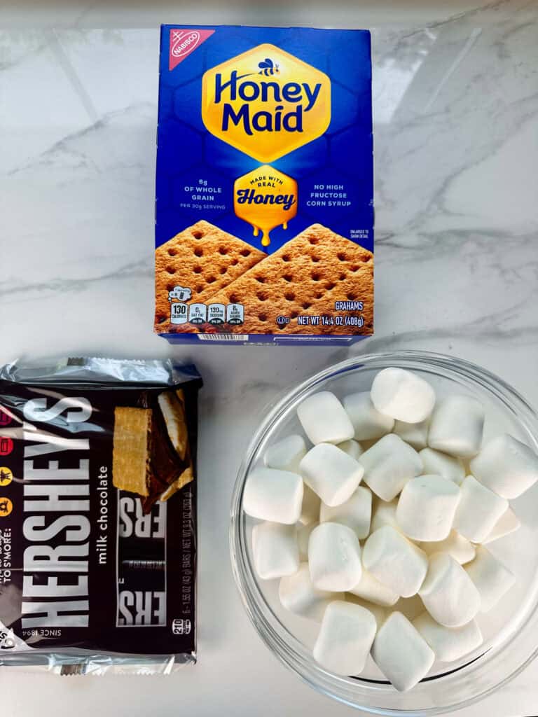 Smores in the oven ingredients on a white background: Hershey milk chocolate bars, large marshmallows, and graham crackers.
