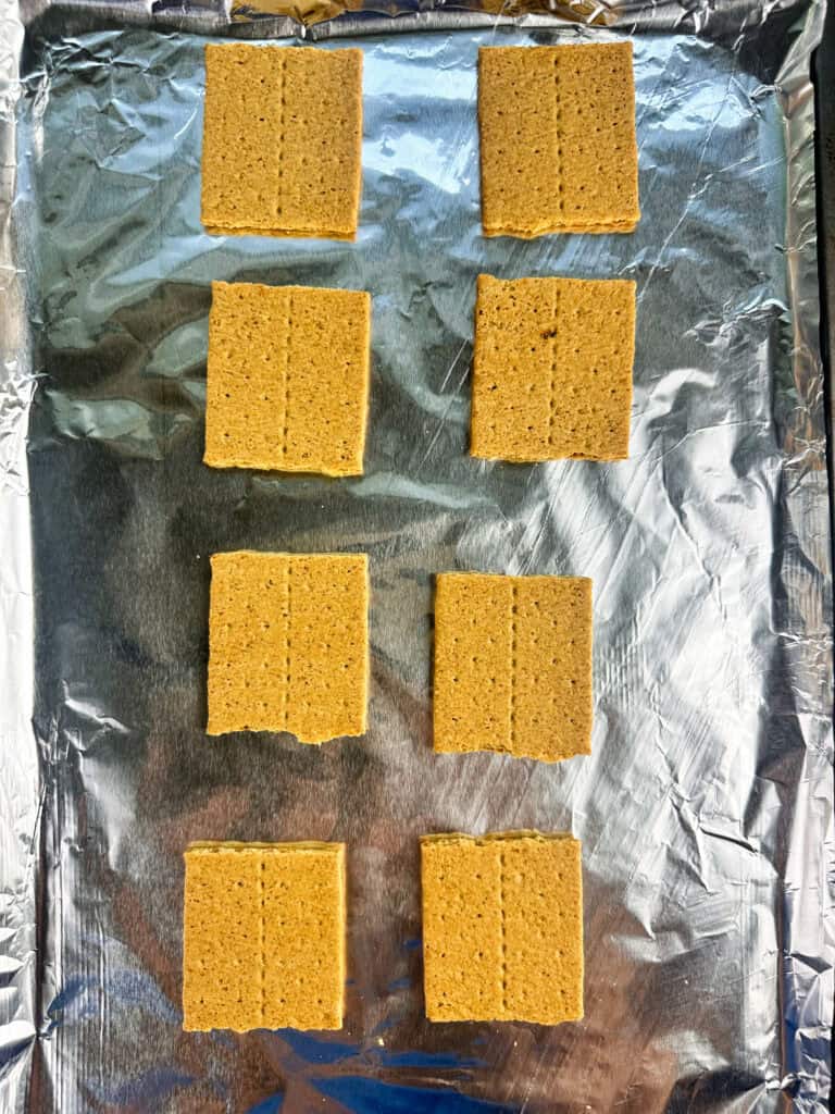 Graham cracker squares arranged on a sheet pan lined with aluminum foil.