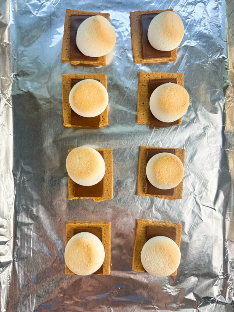 Fully baked sheet pan smores on aluminum foil with golden brown tops.