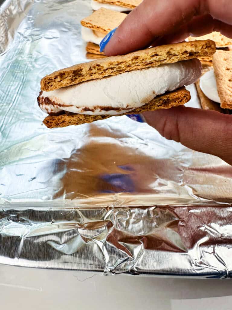Smooshed smore between two fingers with more smores in the background.