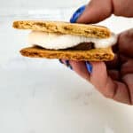 Smooshed smore between fingers with more smores in the background.
